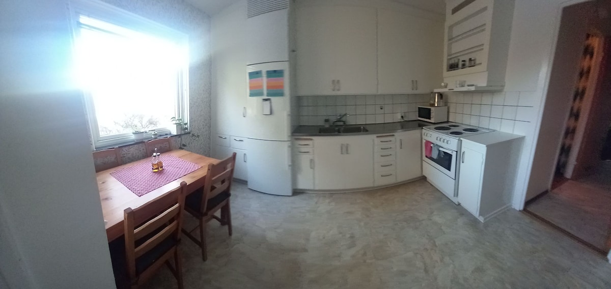 A well-organized kitchen features white cabinets and a spacious countertop. A dining table with wooden chairs is positioned near a window, allowing natural light to fill the room. Kitchen appliances, including a refrigerator, microwave, and stove, are neatly arranged for convenience.