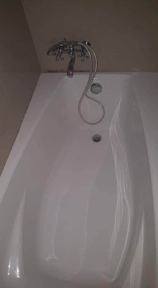 A clean and spacious bathtub is showcased against a neutral wall. A sleek chrome faucet extends above the tub, with a handheld shower attachment visible. The surface of the tub reflects soft light, indicating a serene bathing environment.