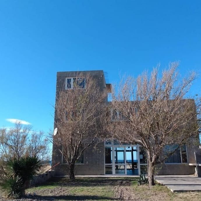 A modern building with a simple architectural design is surrounded by dry landscaping. Large windows are featured on the front, allowing for natural light. A clear blue sky provides a contrasting backdrop, showcasing the structure's height and openness.