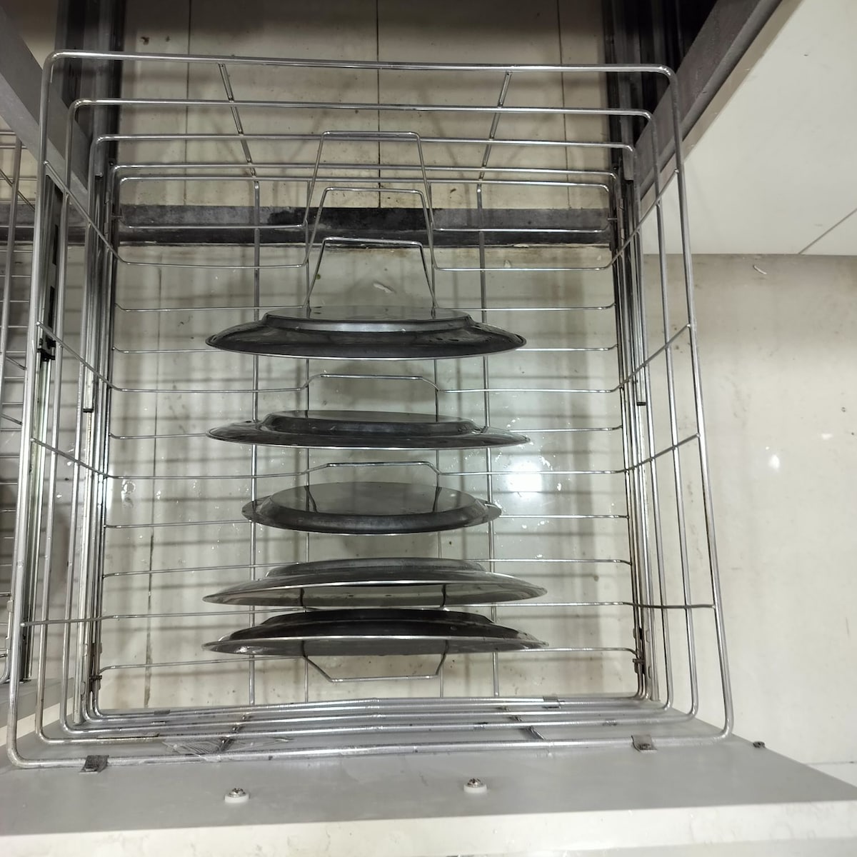 A stainless steel dishwasher rack is filled with neatly arranged platters. Several levels of the rack are visible, showcasing multiple stacked dishes. The interior is lined with a smooth surface, indicating a clean and organized space.
