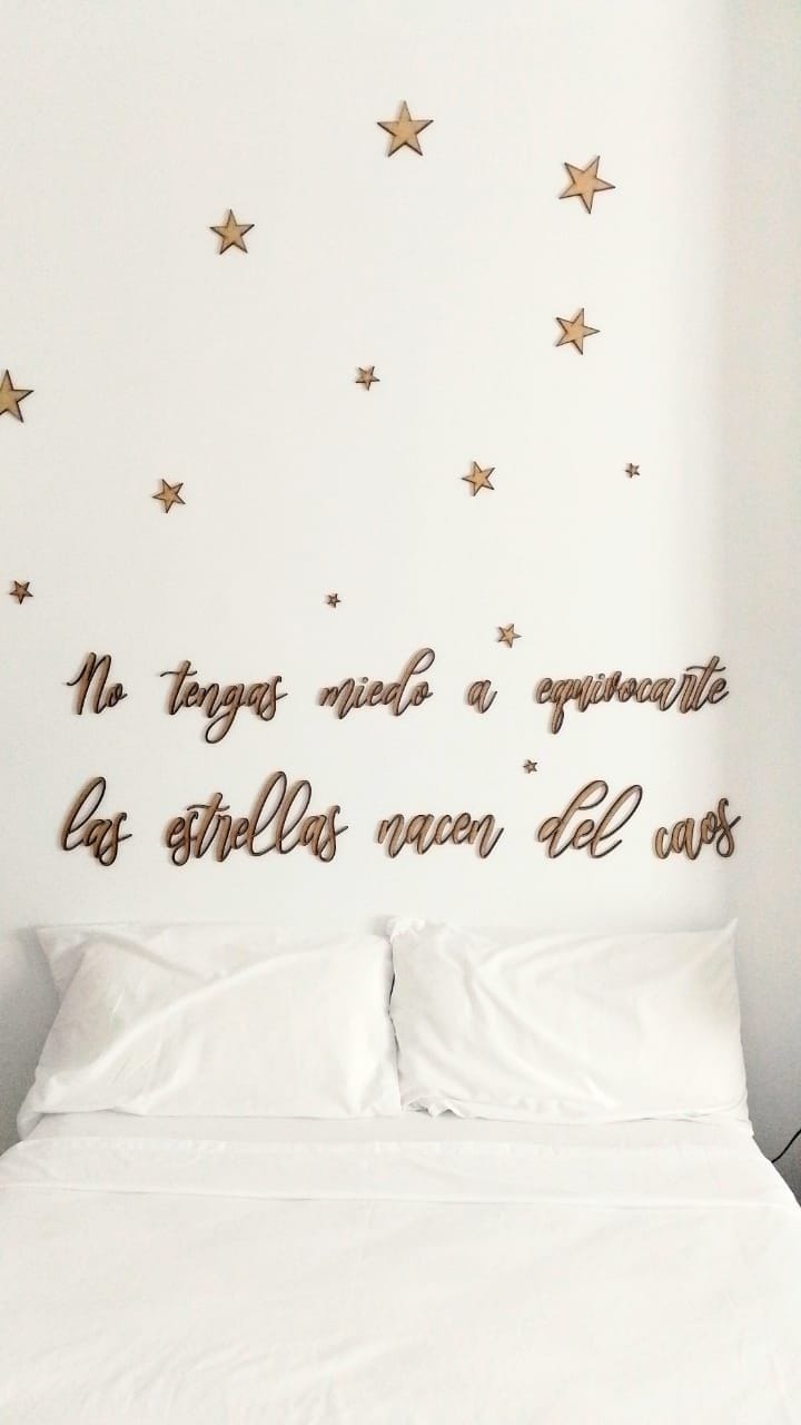 A cozy sleeping area features a spacious bed adorned with soft, white linens. Above, golden stars are displayed on the wall, accompanied by an inspiring message crafted in wood, creating a calming and serene atmosphere.