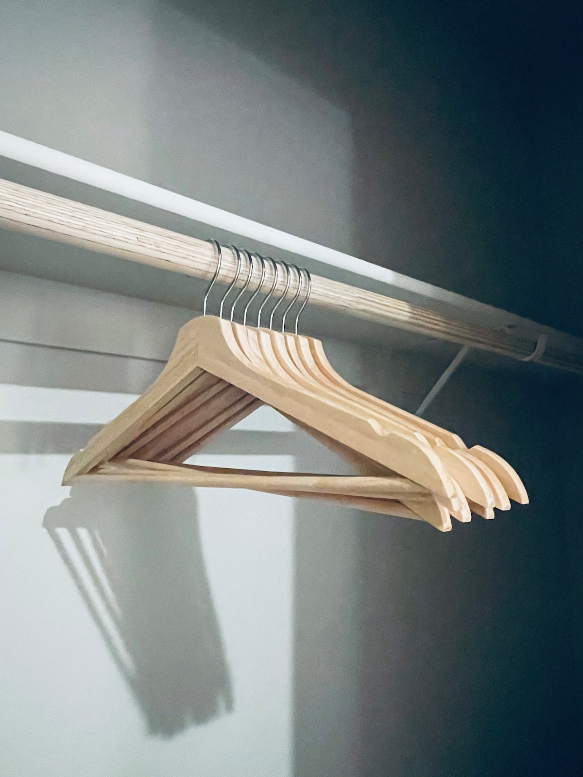 A streamlined closet rod is equipped with several wooden hangers, showcasing a simple design. The light creates subtle shadows on the wall, enhancing the uncluttered and organized appearance of the space.