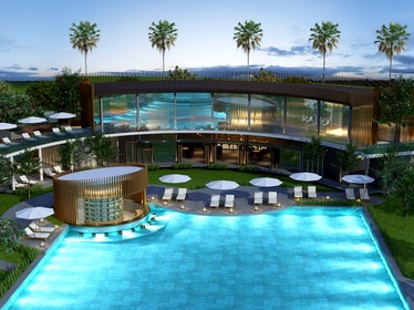 The image features a large swimming pool with clear blue water, surrounded by lounge chairs and umbrellas. A modern building, featuring expansive glass windows and palm trees, is situated in the background, providing a sense of spaciousness and inviting relaxation.