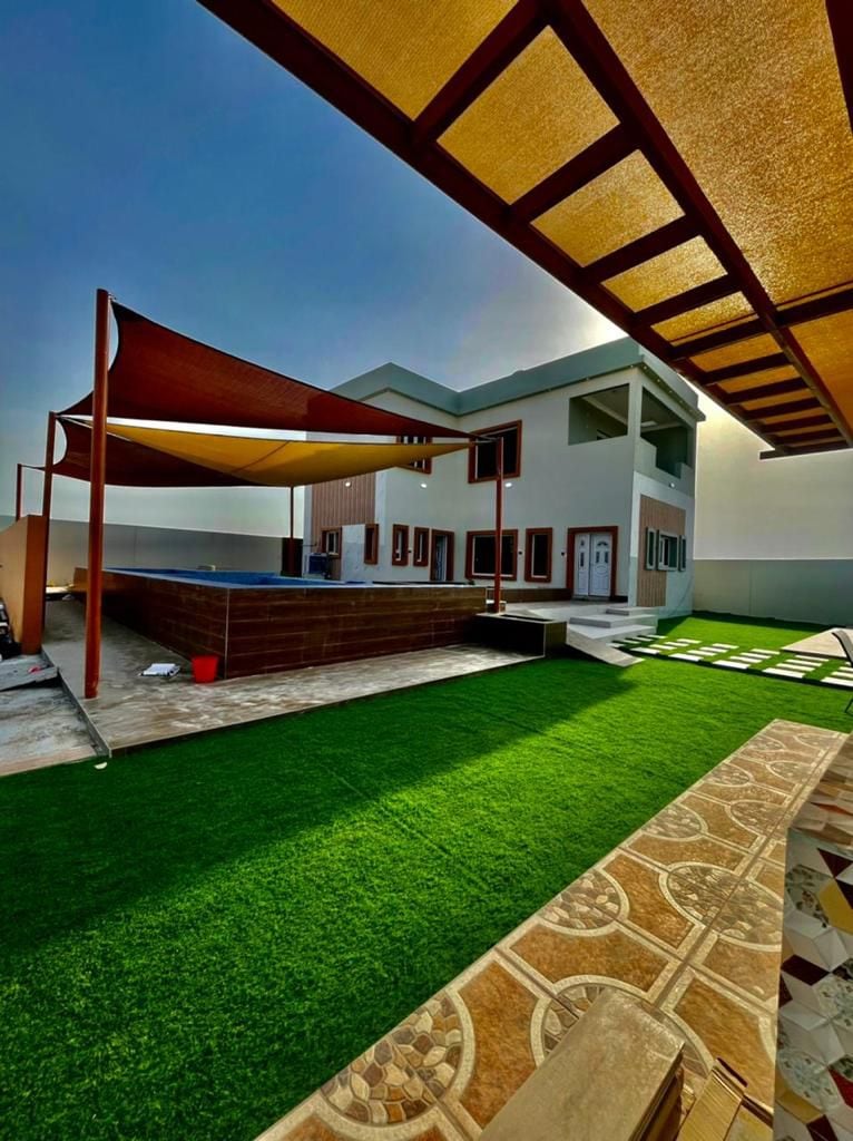 An outdoor space is highlighted, featuring a green lawn adorned with shaded areas from stylish fabric canopies. A pool is visible under the shelter, with a structured patio and a well-constructed house occupying the background.