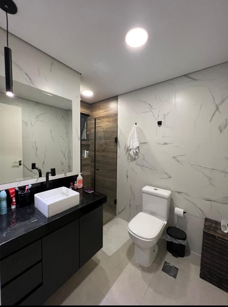 A modern bathroom features sleek black cabinetry and a white vessel sink positioned on a dark countertop. Natural light reflects off the marbled wall tiles. A spacious shower area is delineated by glass, and practical amenities, including a toilet and towel rack, are provided.