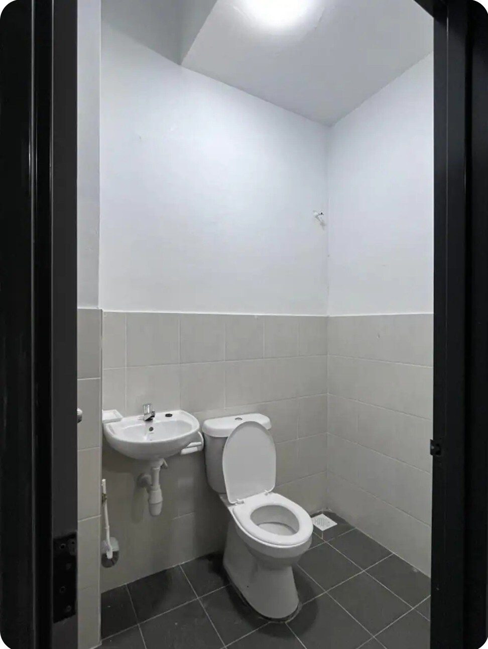 A clean and functional bathroom is depicted, featuring white tiled walls and a modern sink. A white toilet sits against one wall, with light entering from a ceiling fixture above. The flooring is simple black tiles.
