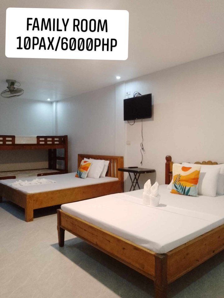 The family room features two spacious beds, one arranged as a double and the other as a bunk. A small table and television are present, while white walls and light-colored flooring contribute to a clean, airy feel.