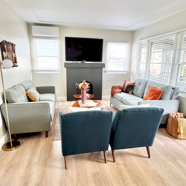 Sala de estar con sofá Sage Green, caja y barril extraíble y sillones para el olmo oeste de mediados de siglo.  Wifi y Amazon FireStick incluidos.  Las ventanas dan al porche delantero con vistas al patio trasero privado.