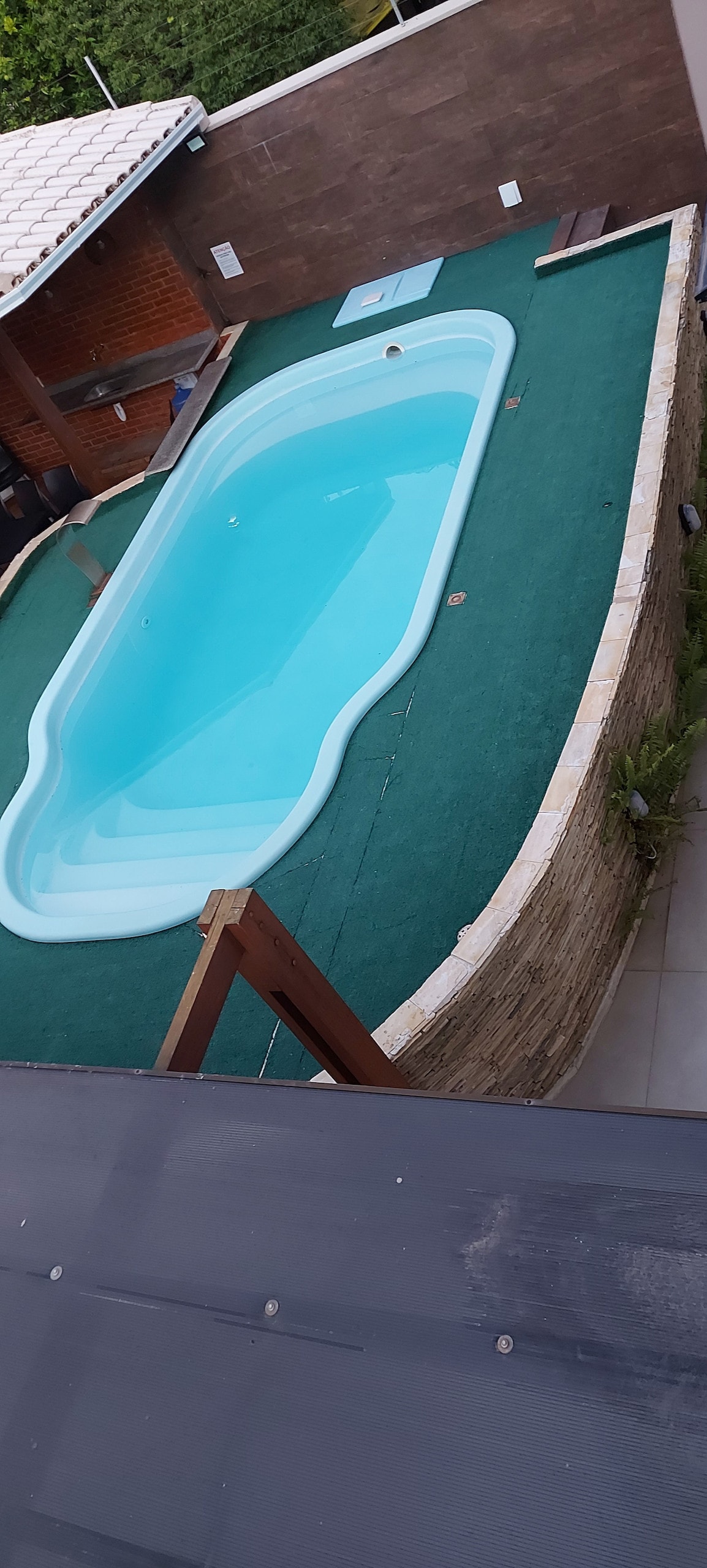 A private swimming pool is featured, surrounded by a green surface and bordered with textured stone. A shaded area with a wooden structure is nearby, providing a relaxing space for outdoor enjoyment.