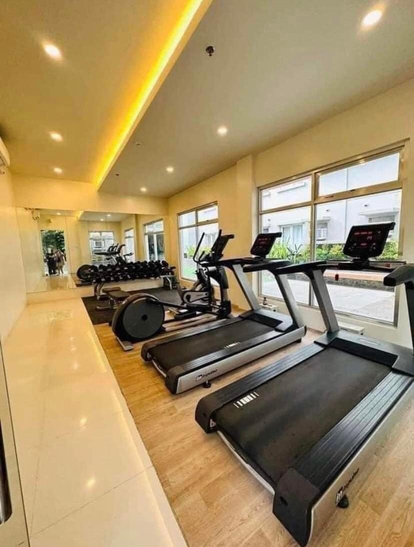 A well-equipped fitness area features multiple treadmills and exercise bikes positioned near large windows. Natural light fills the space, highlighting the sleek equipment and smooth flooring. A mirror across one wall enhances the sense of openness and provides a view of the workout area.
