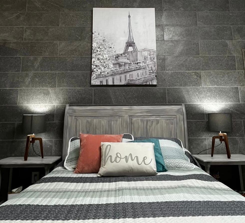 A cozy sleeping area is presented with a spacious bed featuring a striped blanket. Flanking the bed are two wooden nightstands, each with a lamp providing soft lighting. A wall art piece depicting the Eiffel Tower adds a Parisian touch above the bed.