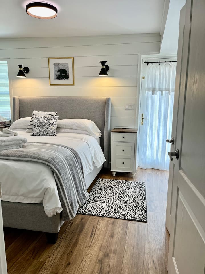 Dormitorio principal con cama tamaño queen, baño de 2 piezas y TV montada en la pared. 