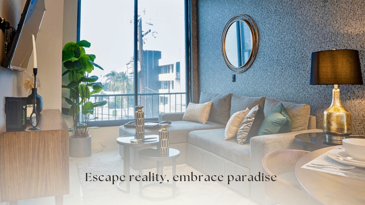 A modern living area features a spacious sofa adorned with decorative pillows, complemented by two stylish side tables. Large windows allow natural light to fill the room, while a potted plant adds a touch of green. A round mirror enhances the sense of openness.