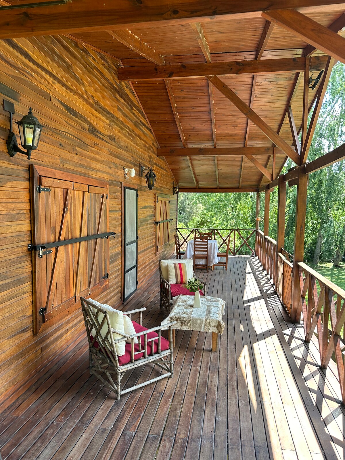 A wooden deck features comfortable seating arrangements, including two chairs and a small table. The space is adorned with natural wood details and overlooks the lush greenery surrounding the property, providing a serene atmosphere for relaxation.