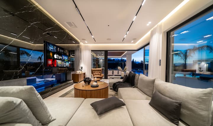 Ground Floor - Sophisticated living area with sleek modern design, a plush sectional sofa, and floor-to-ceiling windows framing sunset views