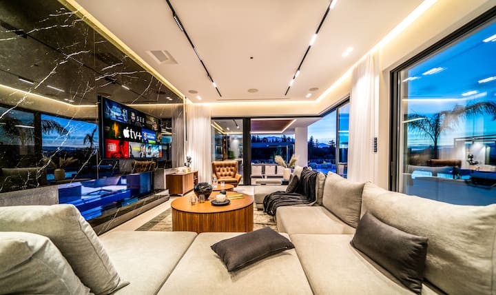 Ground Floor - Sophisticated living area with sleek modern design, a plush sectional sofa, and floor-to-ceiling windows framing sunset views