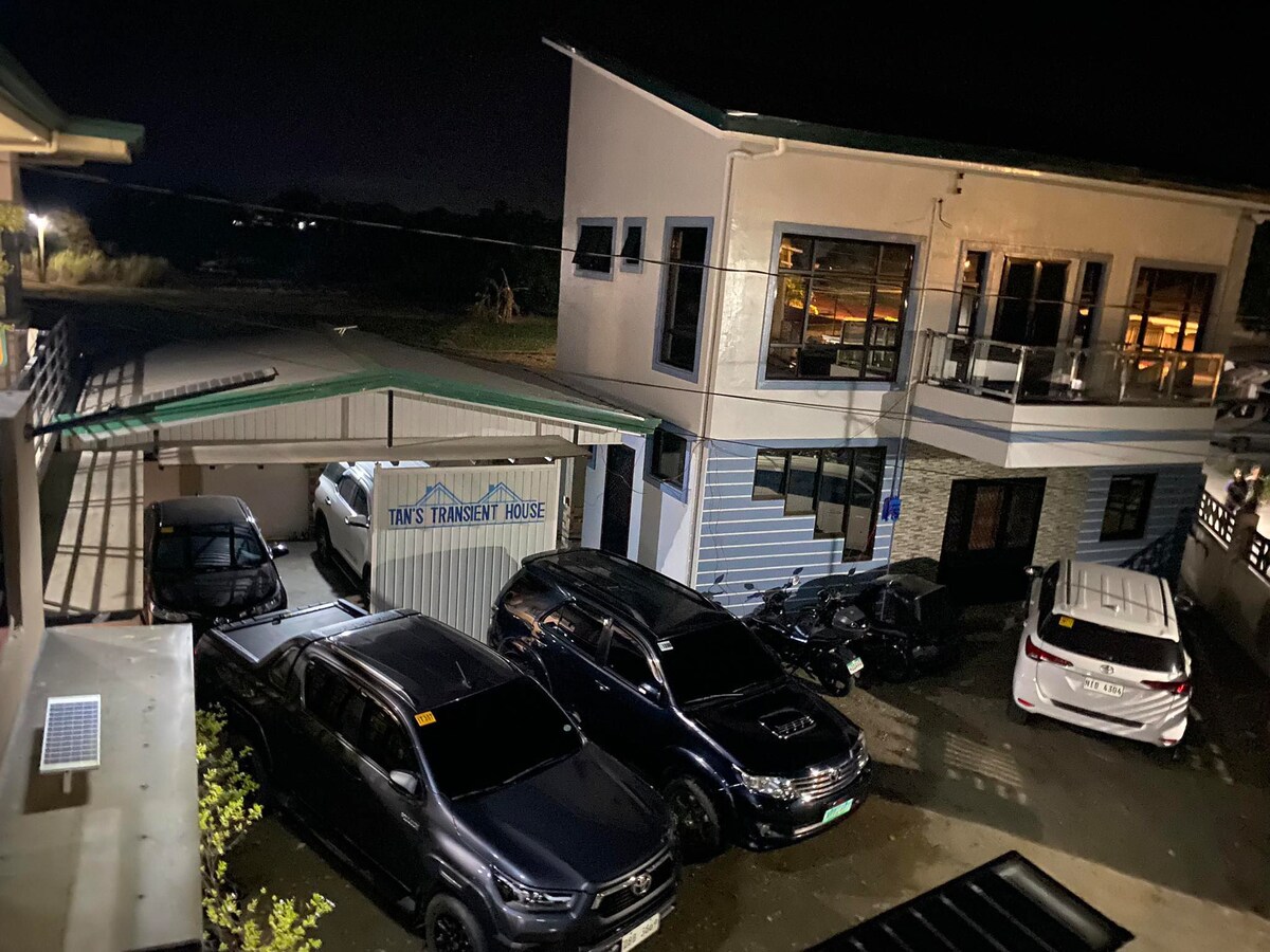 A gated parking area is shown, accommodating multiple SUVs under soft outdoor lighting. The parking space connects to a two-story building featuring large windows. The surroundings indicate a tranquil environment, enhancing the overall peace of the location.