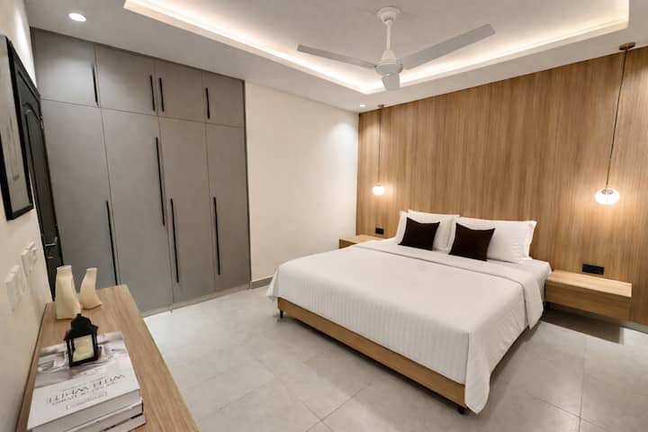 Bedroom 1 - Spacious bedroom with a king-size bed, modern lighting, full-wall wardrobes, and warm wood accents.