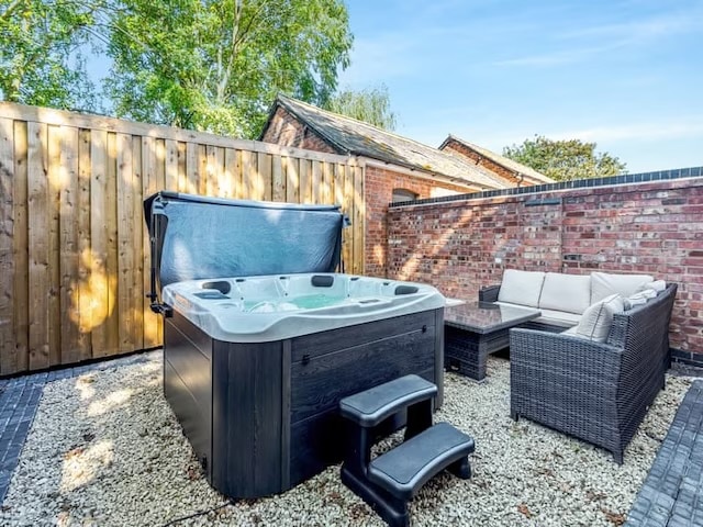 A private hot tub is positioned within a tranquil courtyard, surrounded by wooden fencing and brick walls. A seating area featuring a light-colored sofa accompanies the hot tub, set upon a bed of small white stones, providing a calming outdoor space.