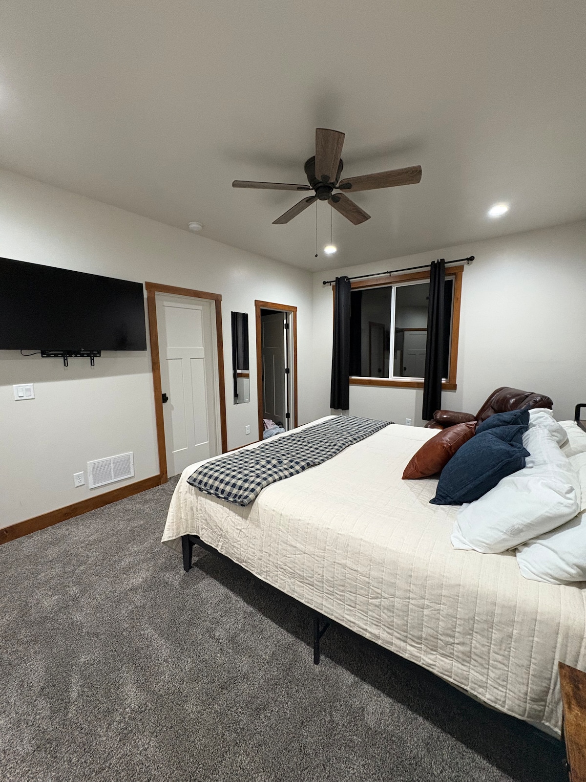 A spacious king bedroom featuring a comfortable king-size bed with crisp linens, accent, and a soft throw. The room includes a wall-mounted TV, a cozy reading chair, and clean, simple décor for a relaxing stay. 