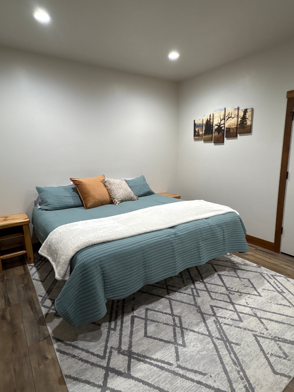A spacious bedroom featuring a king-size bed with soft linens, accent pillows, and a cozy throw. The room includes a large smart TV, wooden dresser, and ample closet space, offering comfort and convenience for a relaxing stay. 