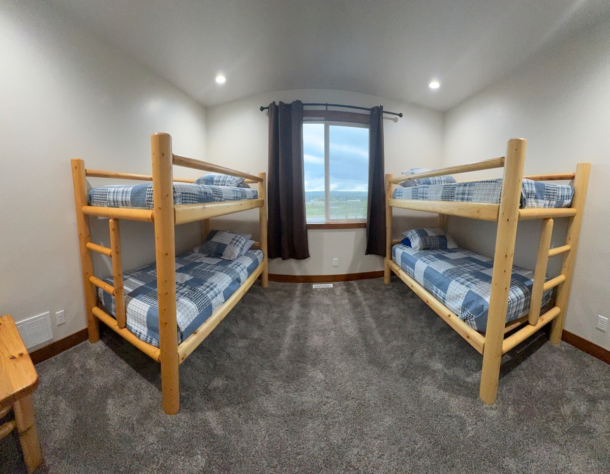 A bright and spacious bunk room featuring two twin-over-twin log bunk beds with cozy bedding. This setup is perfect for kids, teens, or groups who want to share a fun and comfortable space.