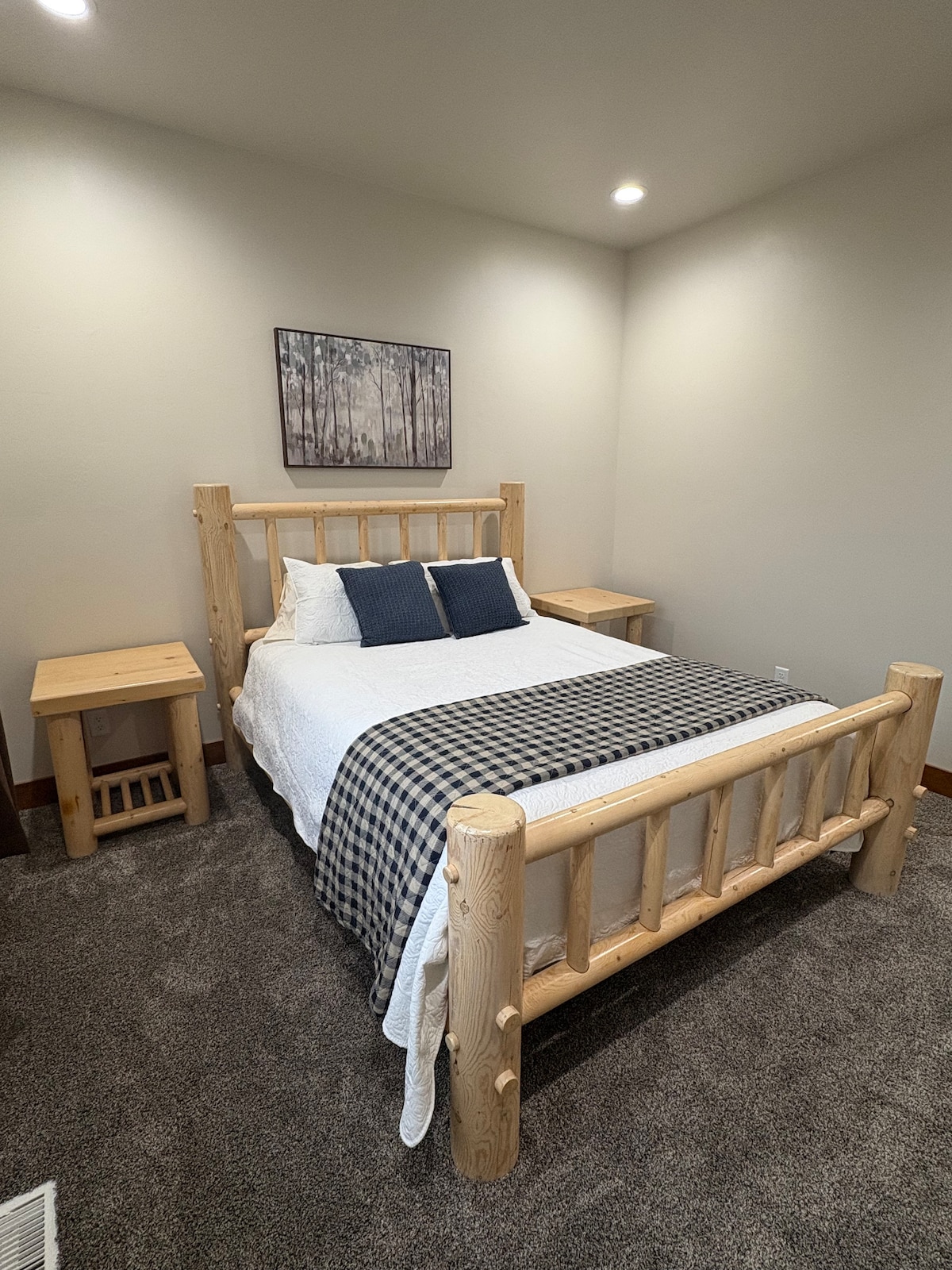 A cozy room with a queen-size log bed, soft linens, two pillows, a patterned throw blanket, and matching wooden nightstands. Simple, clean, and comfortable—perfect for a restful stay. 