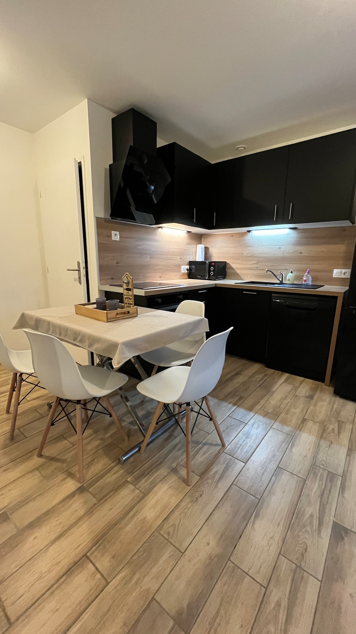 A modern kitchen area features dark cabinetry and wood accents, complemented by a dining table surrounded by white chairs. Essential appliances, including a microwave and coffee maker, are visible, providing a functional space for meal preparation and dining.