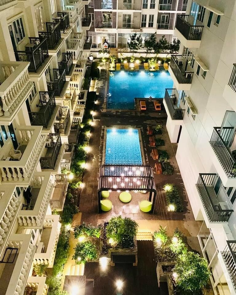 An aerial view showcases the well-lit courtyard of the condo complex, featuring a spacious swimming pool surrounded by lounge chairs. Lush greenery and illuminated pathways enhance the inviting atmosphere, while modern seating areas are positioned along the sides of the pool.