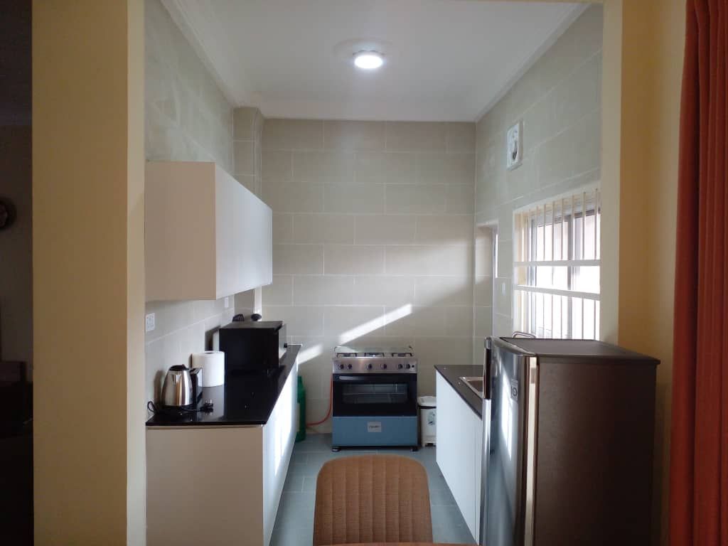 The kitchen is equipped with modern appliances, featuring a refrigerator, oven, and kettle. Counter space is provided for food preparation, with ample storage cabinets above and below. Natural light enters through a window, creating a bright environment.