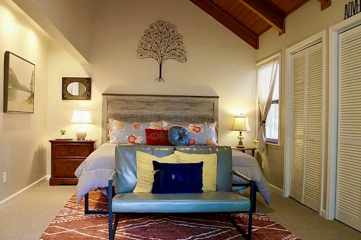 Dormitorio tamaño king con baño privado con ducha, armarios grandes, sala de estar con puerta corrediza de vidrio y vistas a la terraza y a las copas de los árboles.