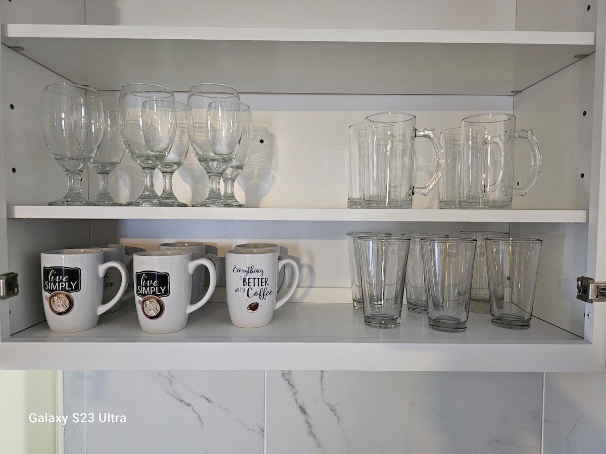 A well-organized kitchen cabinet displays a selection of glassware. The top shelf holds several elegant wine glasses and two large mugs. The bottom shelf features an assortment of tall glasses and additional drinking cups, all neatly arranged for convenience.