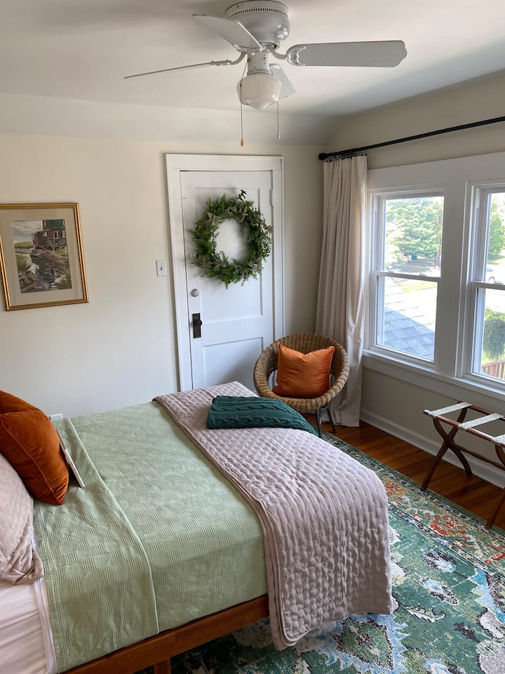 Прекрасна спална соба на вториот кат со вентилатор на вториот кат со тавански вентилатор, стол, плакар, гардеробер, полица за багаж, преносен вентилатор, дополнително ќебе и затемнети кадифени завеси.  Уметничкото дело е на Фриц Морисон, прекрасен уметник од Квинси.  