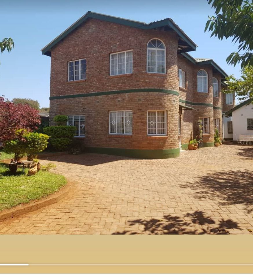 A two-story brick house is set within a landscaped yard featuring neatly trimmed bushes and small trees. Large windows, framed in white, allow natural light to fill the interior. A stone pathway leads to the entrance, enhancing accessibility.