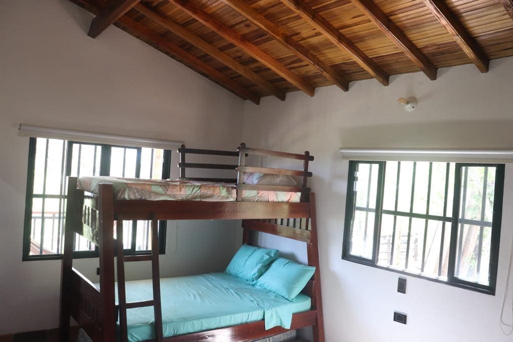 Izba s poschodovými posteľami, manželskou posteľou a jednolôžkom na poschodí a ďalším jednolôžkovým matracom vnútri, so skriňou a ventilátorom.