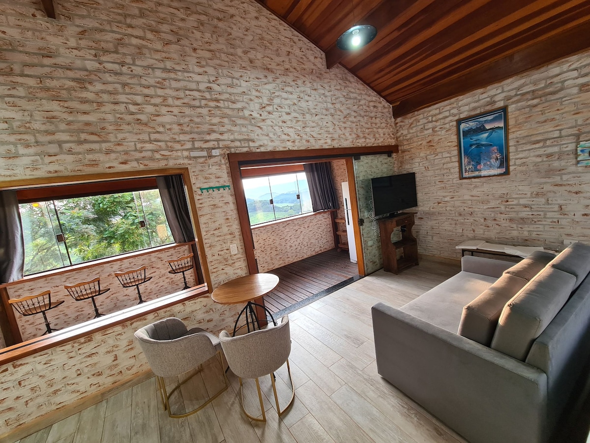 An inviting living space features large windows with mountain views, allowing natural light to fill the area. A comfortable sofa is complemented by two armchairs and a round table. The textured wall adds warmth, while a television is mounted for entertainment.