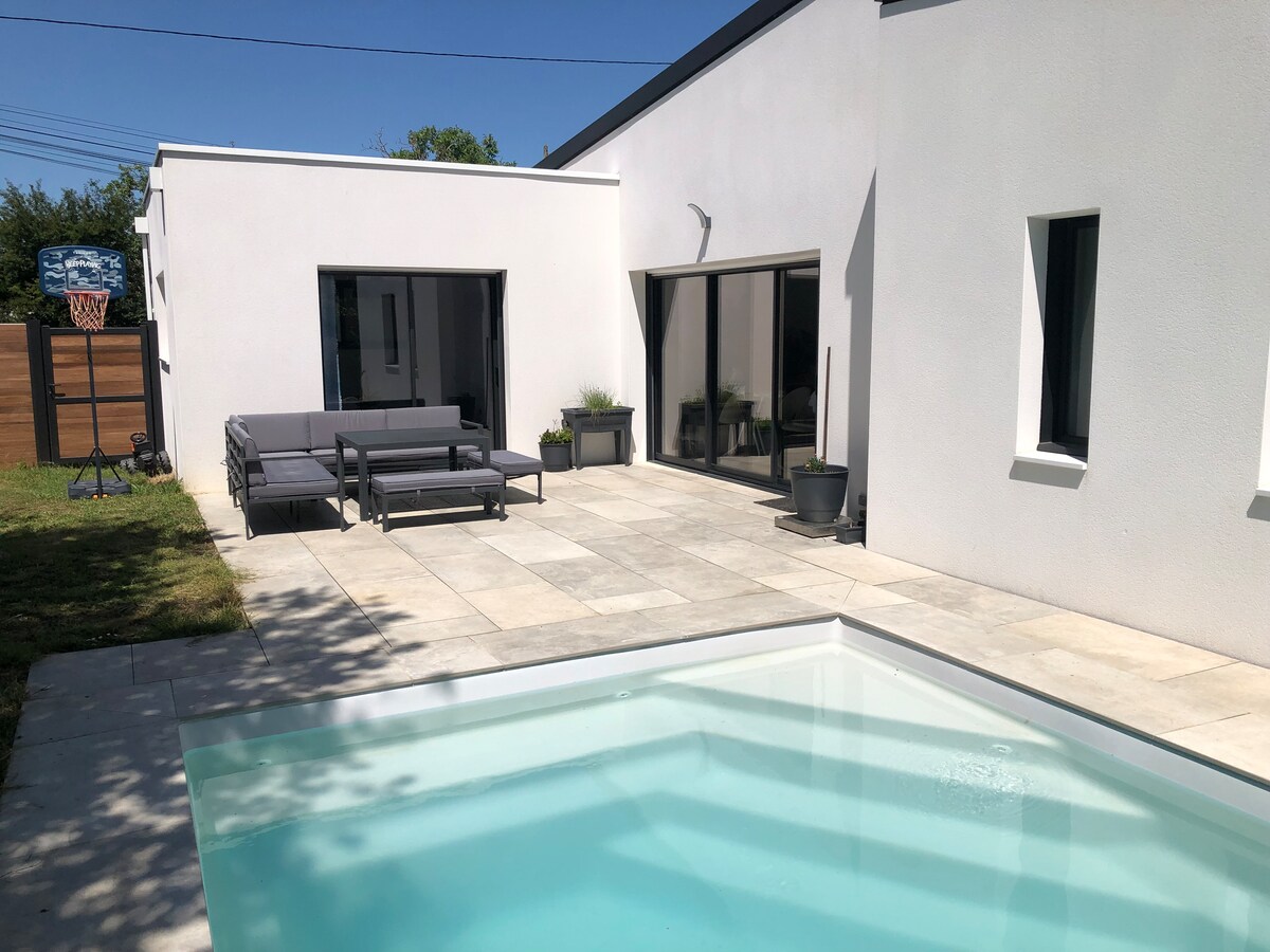 An outdoor area features a modern swimming pool with a clear, inviting surface. A spacious patio includes comfortable seating arrangements, surrounded by landscaped greenery. Large glass doors provide access to the interior, allowing for natural light to fill the space.