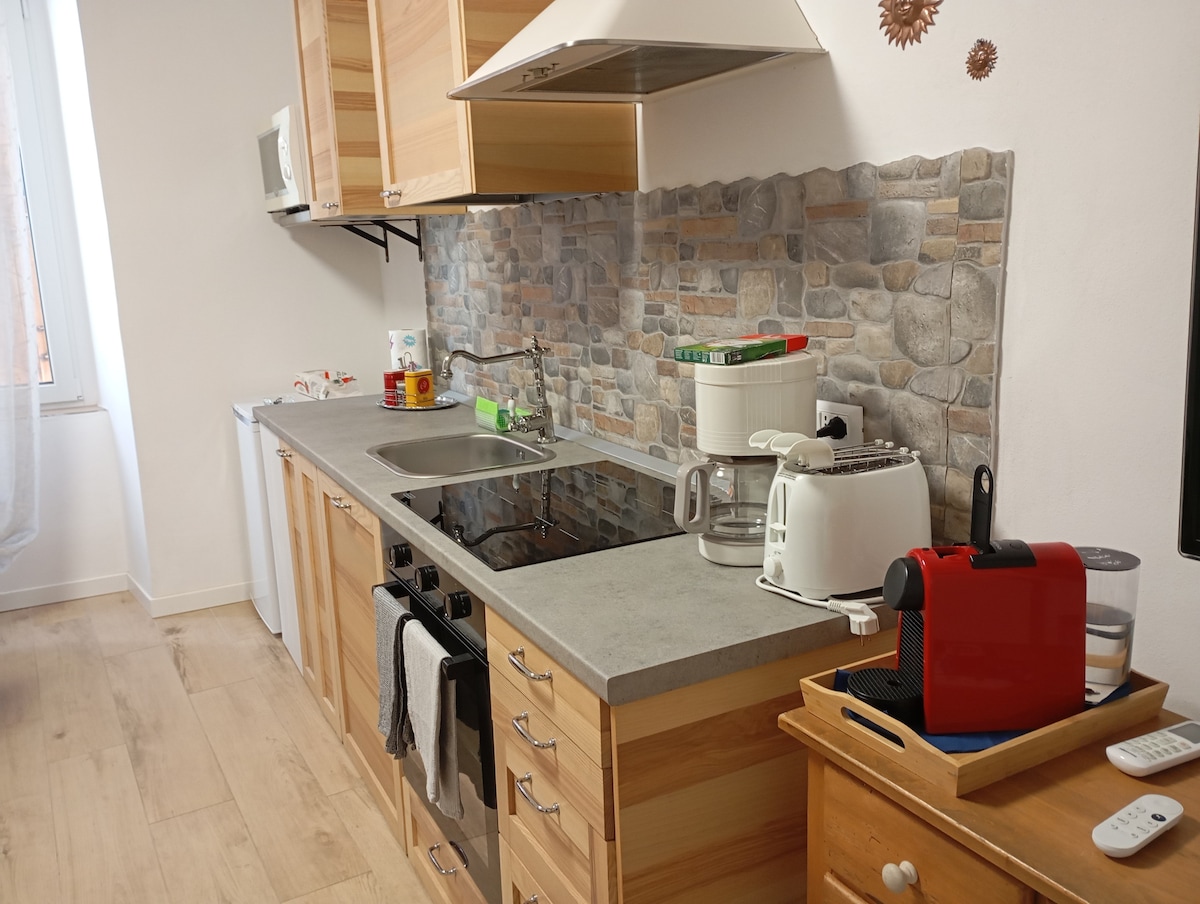 The kitchen area features wooden cabinetry and a stone backsplash. A stainless steel sink and modern appliances, including a toaster, coffee maker, and microwave, are visible. Cooking utensils and pantry essentials are neatly arranged, providing a functional space for meal preparation.