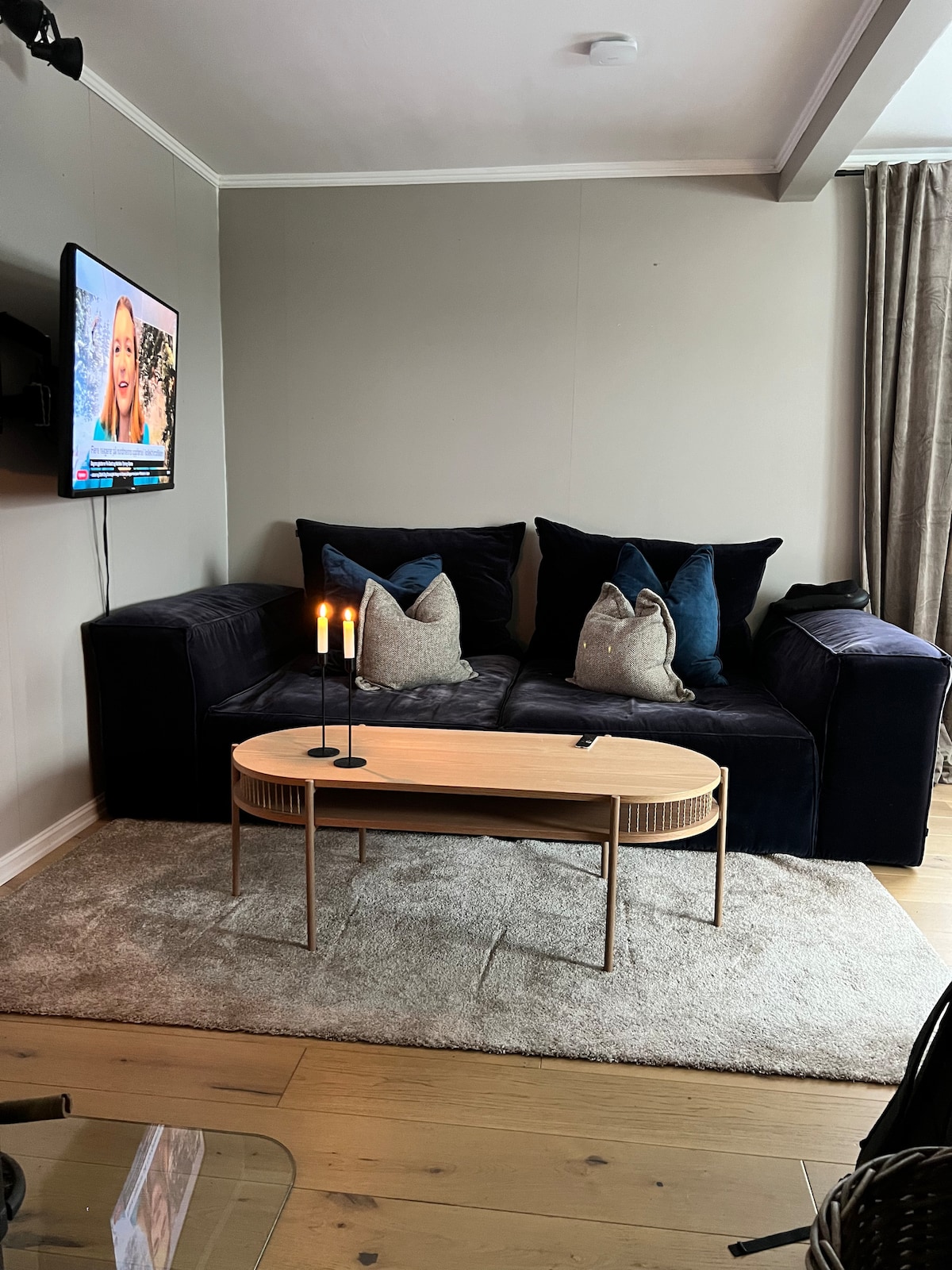 A comfortable seating area features a dark blue couch adorned with decorative pillows in various textures. A round coffee table is placed in front, accompanied by two lit candles, creating a cozy ambiance. A television is mounted on the wall, providing entertainment.