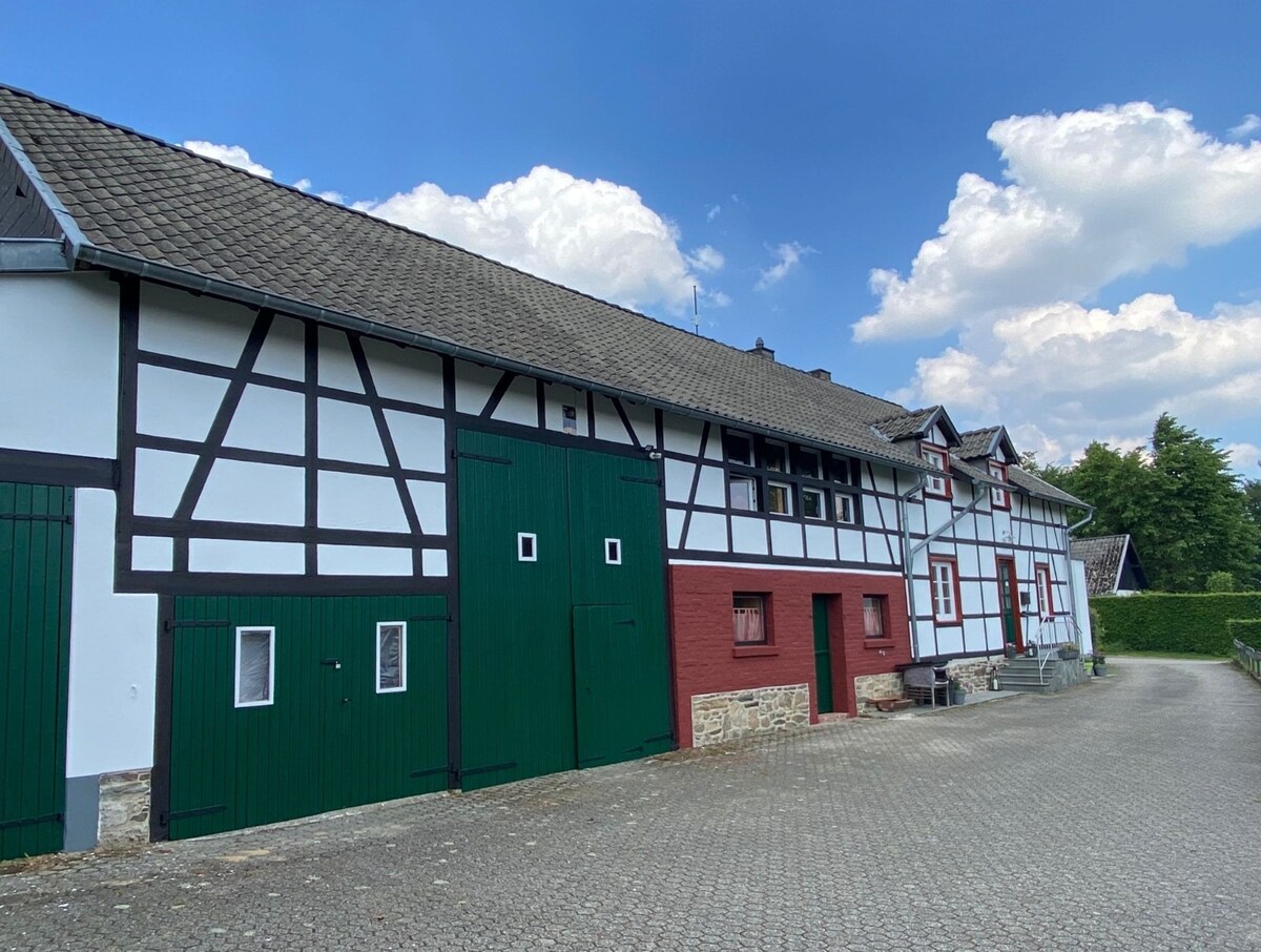 A spacious, traditional building features a blend of white and dark wood accents, with green doors and windows adding a vibrant touch. The exterior is complemented by a paved area, providing ample space for outdoor activities or gatherings.