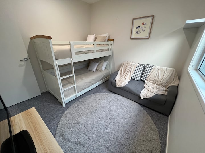 Dhomë fëmijësh me krevate tek, televizor për të luajtur playstation dhe divan.