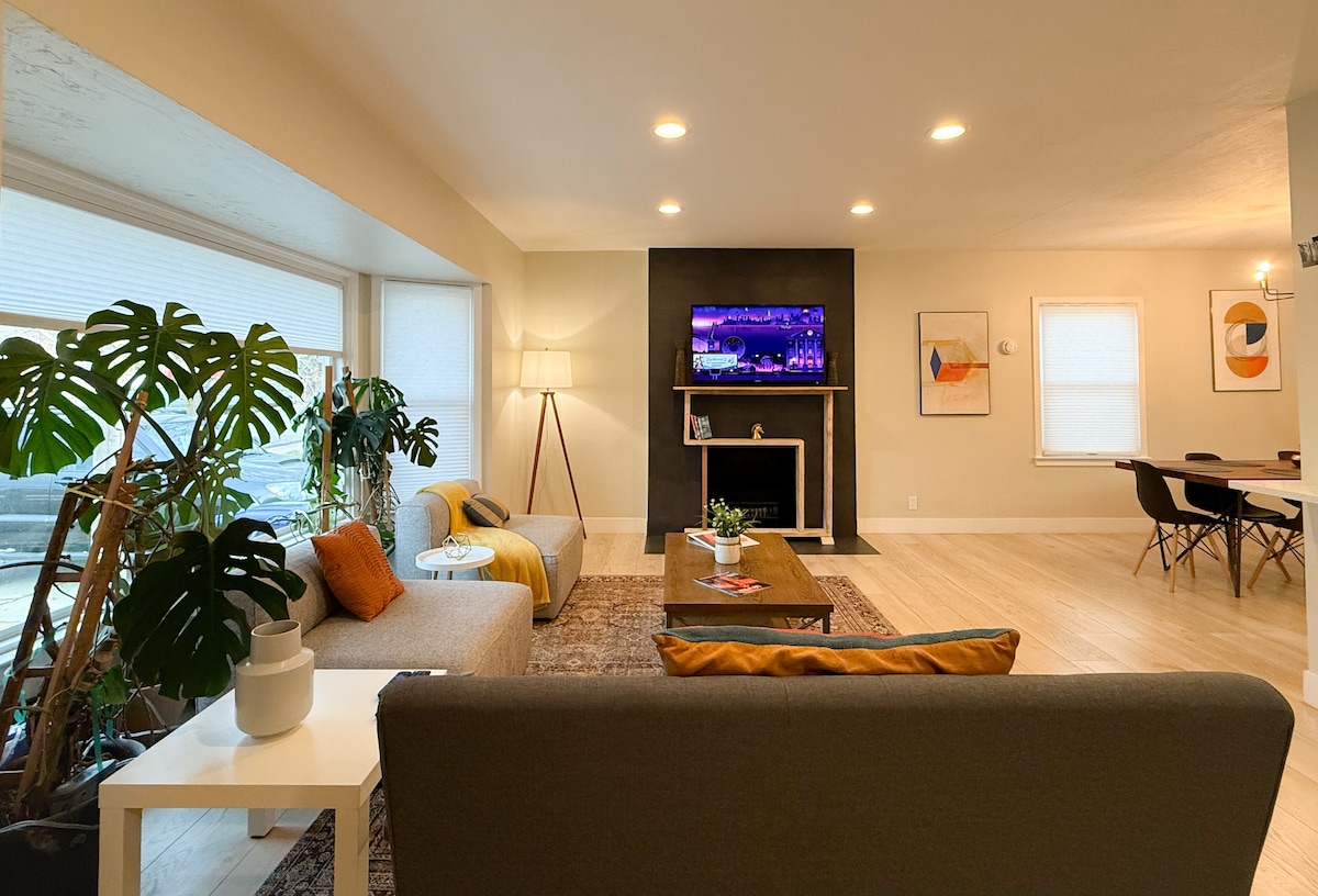 غرفة معيشة بها نباتات حية وكرسيان وأريكة وتلفزيون ذكي ومدفأة مزخرفة