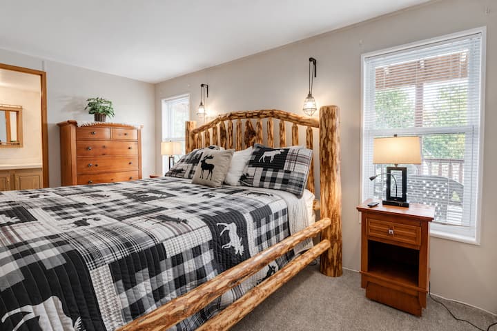 Enjoy restful nights in this spacious bedroom featuring a handcrafted log bed, wildlife-themed bedding, dual nightstands, and soft natural light from two windows. A perfect blend of rustic charm and comfort for your mountain stay