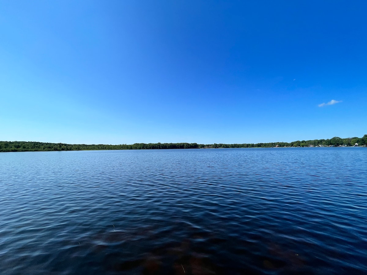 A wide view of Robinson Lake is presented, featuring calm, shimmering water under a clear blue sky. The lush green shoreline is visible in the distance, providing a serene backdrop for outdoor activities.