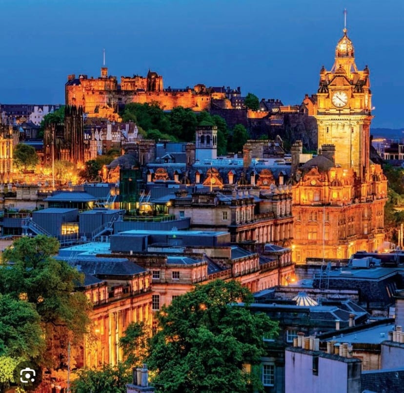 The image captures a panoramic view of Edinburgh at dusk, featuring the illuminated Edinburgh Castle on the hilltop. The skyline is enhanced by the striking clock tower of the Balmoral Hotel, surrounded by charming buildings and greenery, showcasing the historical architecture of the city.