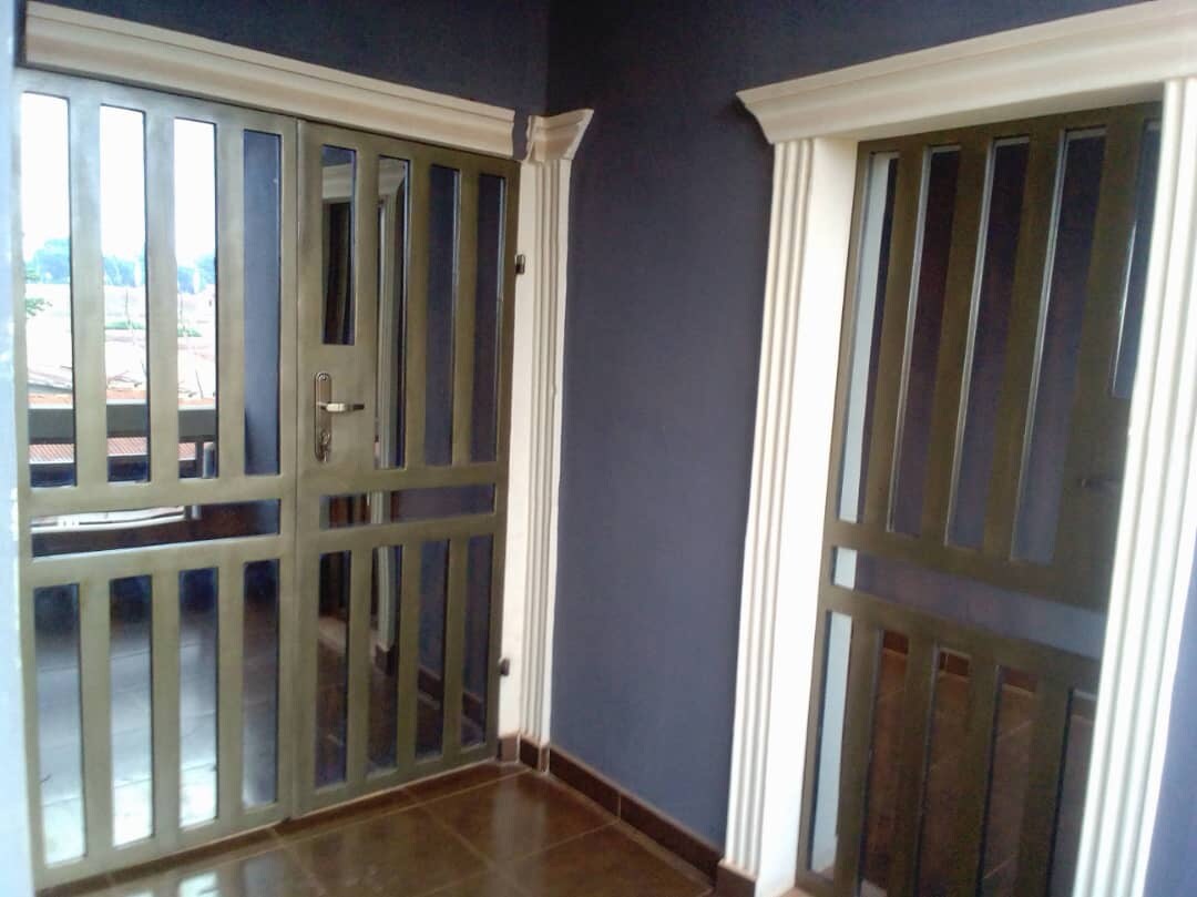 A secure entryway is depicted, featuring double metallic doors with horizontal bars. The space is surrounded by a dark-colored wall and tiled flooring, ensuring a modern aesthetic. Natural light is visible beyond the doors, suggesting an inviting atmosphere just outside.