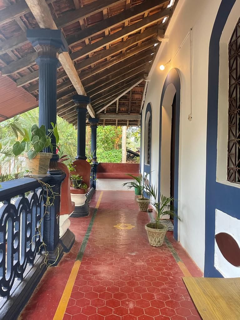 A covered porch area is showcased with a terracotta tiled floor and traditional wood beams overhead. Potted plants line the space, while archway entries lead to the interior rooms. Warm lighting enhances the inviting atmosphere of this serene corridor.