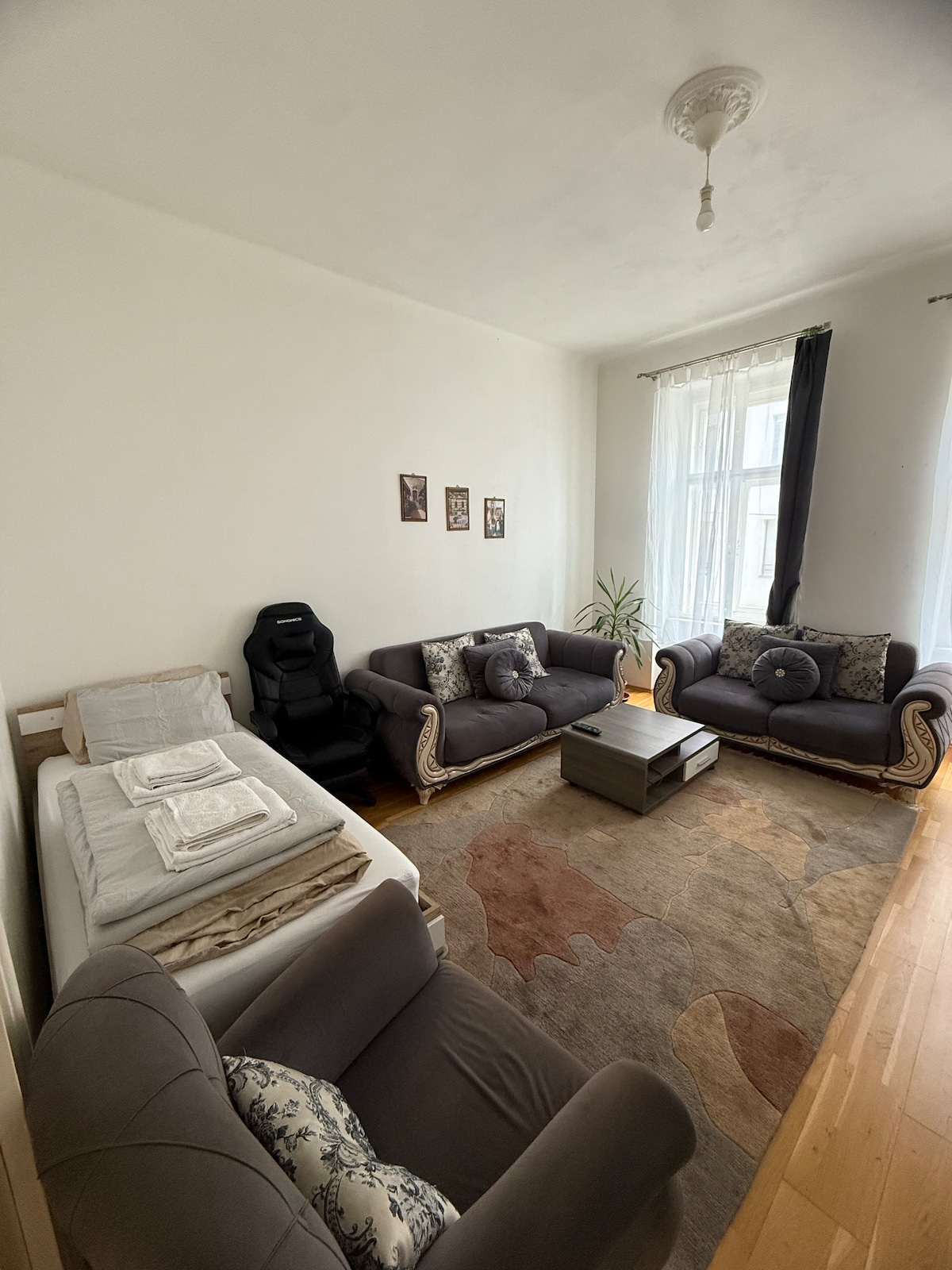 A cozy living area is presented with two elegant sofas and a modern coffee table. A plush armchair adds to the seating options. Sunlight filters through the large windows, enhancing the space's calm atmosphere. An indoor plant brings a touch of greenery to the room.