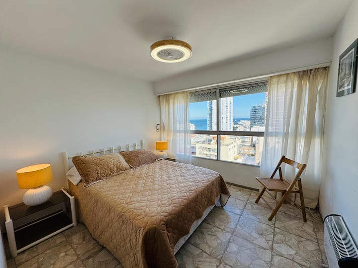 Priestranná spálňa s manželskou posteľou. Veľká úložná skriňa. Nočné stolíky s lampami. Elektrický sporák a stropný ventilátor.