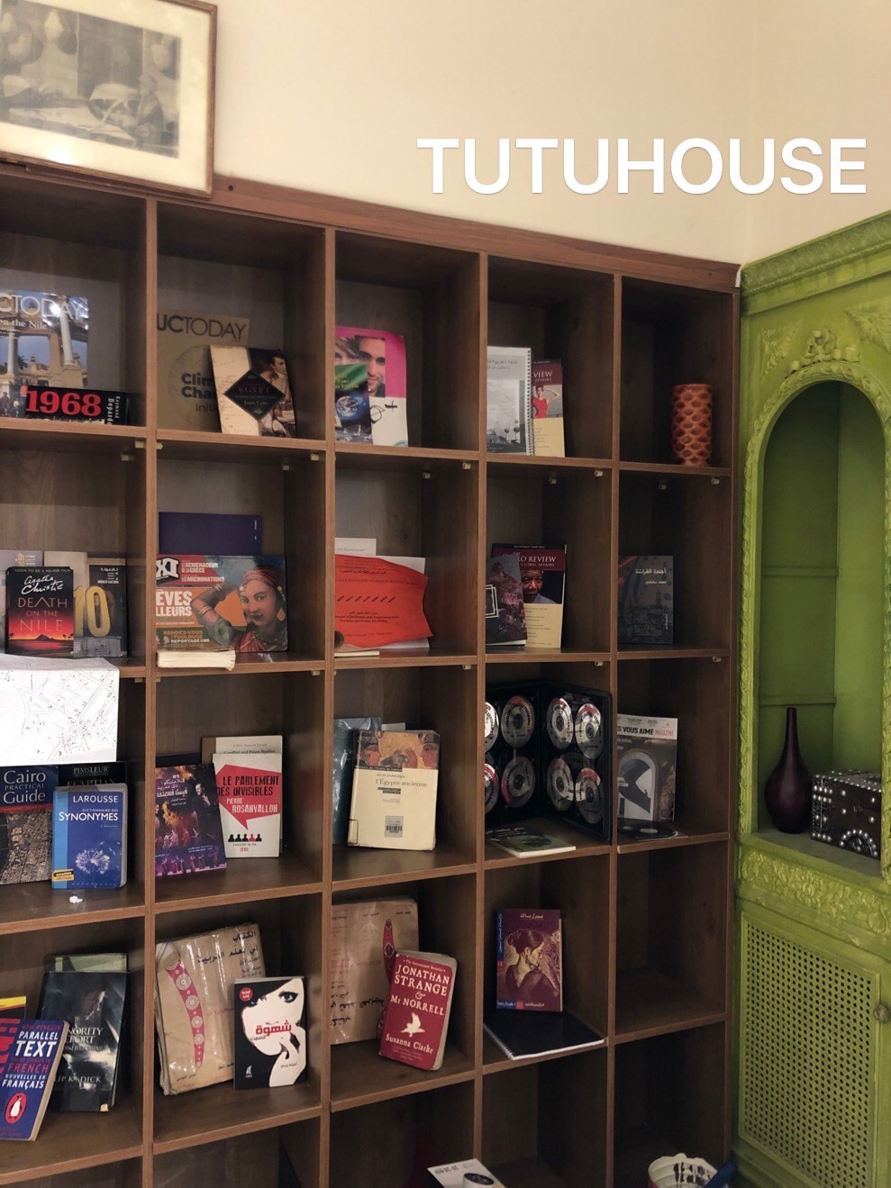 A wooden bookshelf is filled with a variety of books covering different topics, arranged neatly within cubby compartments. Decorative items and plants are placed on some shelves, adding a touch of vibrancy to the space.